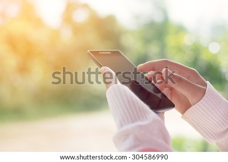 Female using mobile smart phone outdoor, nature background. (vintage color tone)