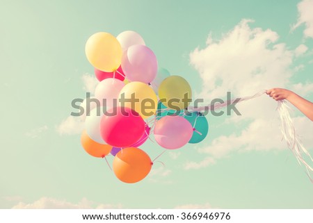 Girl hand holding multicolored balloons done with a retro vintage instagram filter effect, concept of happy birthday in summer and wedding honeymoon party (Vintage color tone)