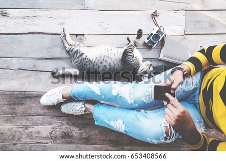 Hipster lifestyle - Girl in jeans with black smart phone and retro camera with cat sit on the wooden floor. vintage film color effect and retro color style