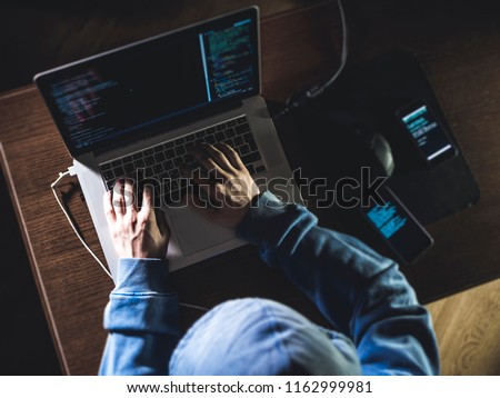 overhead hacker in the hood working with laptop and mobile phone typing text in dark room
