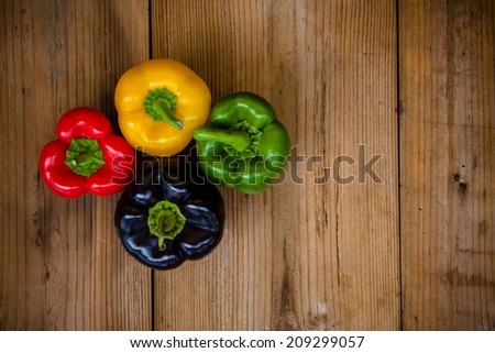 Red, green, black and yellow bell peppers on wooden background