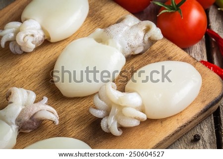 Raw babies cuttlefish  on a cutting board with tomatoes and chili peppers closeup