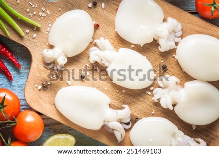 Raw babies cuttlefish  on a cutting board with tomatoes, onions, chili peppers and lemon closeup