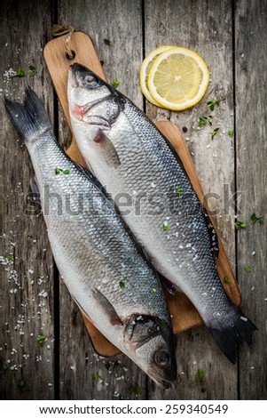 two raw fresh sea bass on a cutting board with lemon and sea salt on wooden rustic table