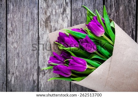 bouquet of purple tulips in a kraft paper on a rustic background closeup