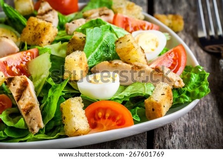 Caesar salad with croutons, quail eggs, cherry tomatoes and grilled chicken closeup on dark background