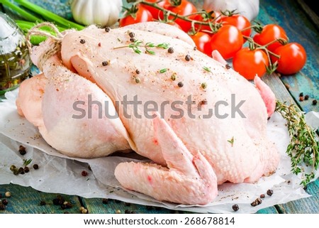 organic raw whole chicken with thyme, cherry tomatoes on a rustic wooden table