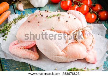 organic raw whole chicken with thyme, tomatoes, carrots and garlic on a rustic wooden table