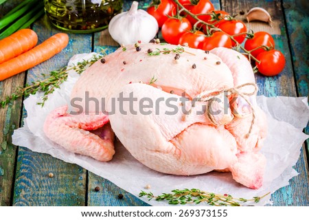 organic raw whole chicken with thyme, tomatoes, carrots on a rustic table