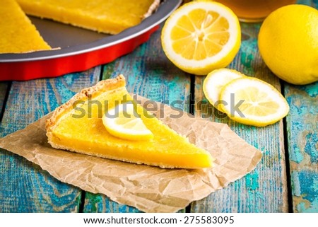 piece of lemon tart on abaking paper with lemons on rustic blue table