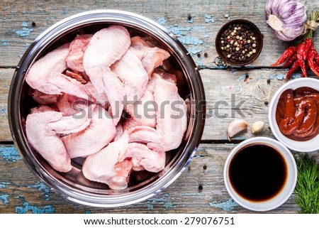 Fresh raw chicken wings in a bowl with the garlic, soy sauce and tomato paste on rustic table