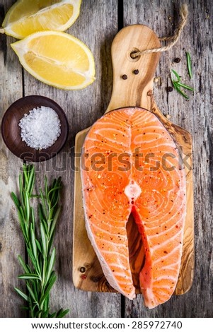 fresh raw salmon steak with salt, lemon, and rasemary on the rustic wooden table