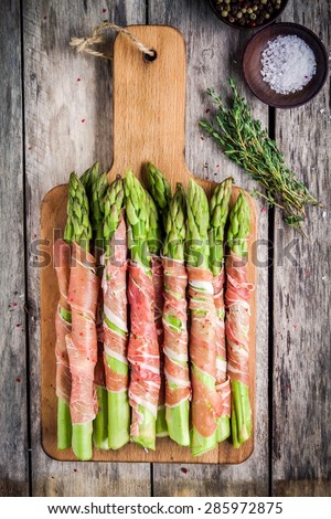 Fresh organic asparagus wrapped in Parma ham on a cutting board top view