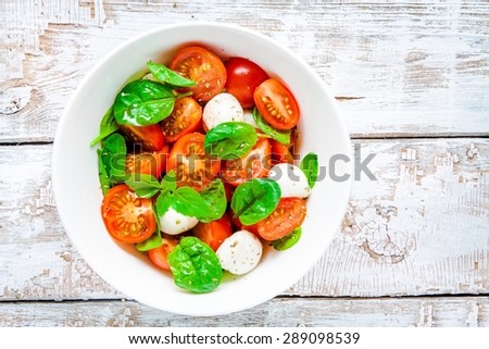 salad of mozzarella, cherry tomatoes and spinach on a white rustic table