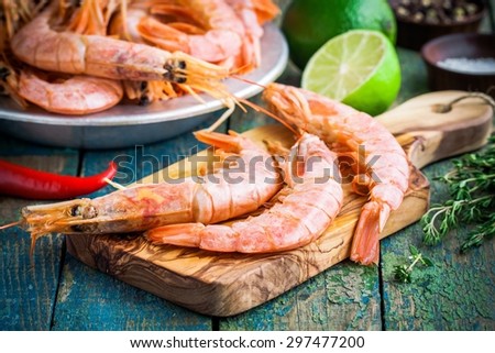 fresh raw prawns on a wooden cutting board with salt, pepper, lime on a rustic table