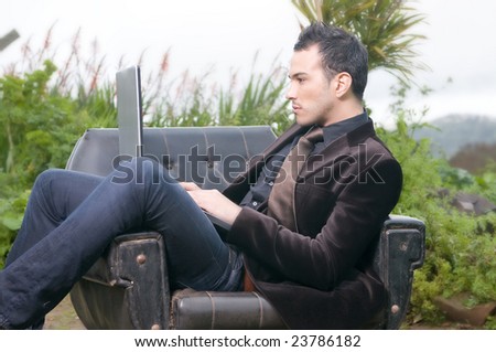 beautiful man with laptop sitting in an armchair in the forest