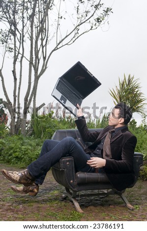 beautiful man with laptop sitting in an armchair in the forest