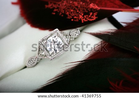 A closeup of an engagement ring in a jewelry case with red feathers.