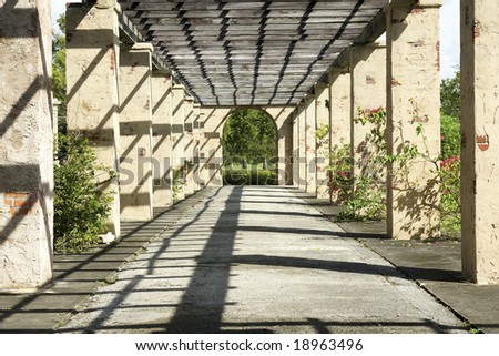 Walkway to the park between columns and under a luminous roof.