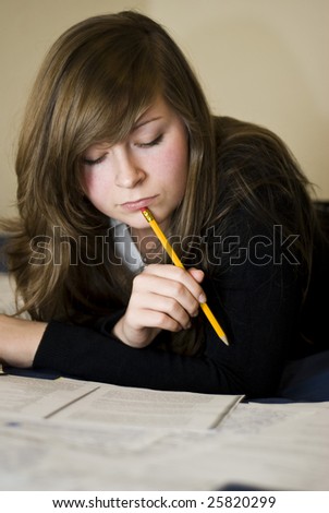 natural young woman reading book on a bed with pencil in her mouth