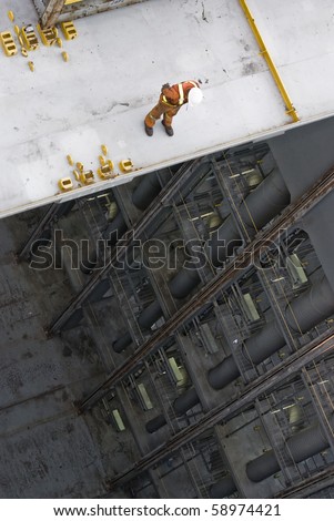 man working over precipice aboard container ship during cargo operation in port terminal