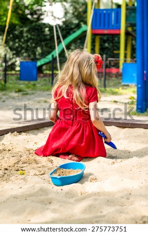 blond girl with long hair rear view playing in sandpit