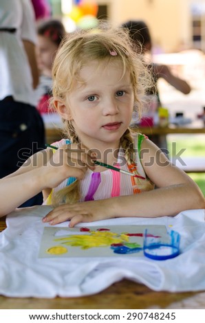 beautiful blond girl painting with brush into t-shirt with colorful colors