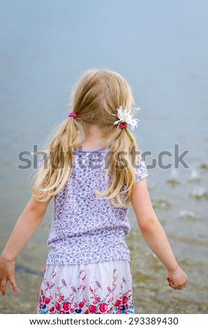 girl with long hair throwing stones into water back view