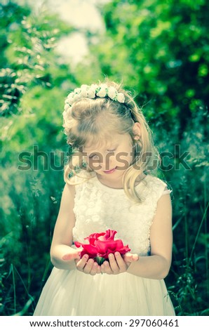 beautiful blond little girl with flower headband holding red rose held in hands