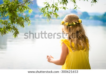 beautiful blond girl in yellow dress with flower headband by the river strand back view