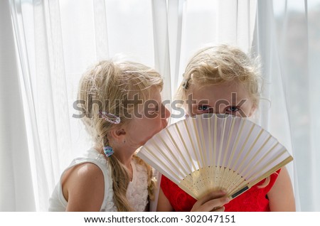 beautiful blond child with long hair in red and white dress among white curtain