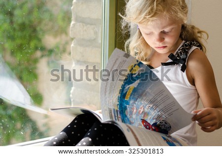 adorable scholar blond girl sitting by the window and reading book