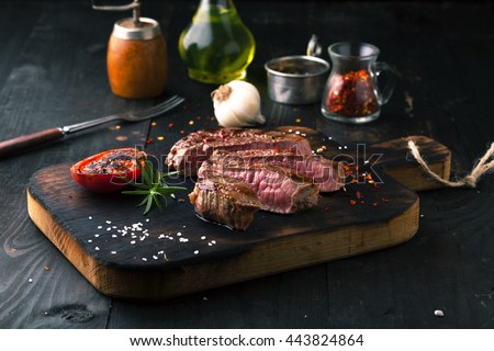 Sliced medium rare grilled Steak Ribeye with rosemary on a dark background