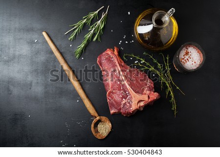 Raw Steak T-Bone with salt and a sprig of oregano and rosemary on a dark background