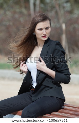 Young woman in the park. Dark hair girl in black suit sitting on bench in park looking at camera