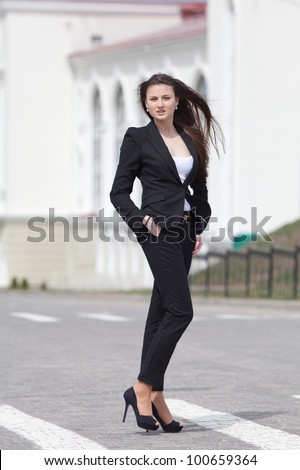 Brunette on stiletto heels outdoors. Young woman in black suit walking along the crosswalk