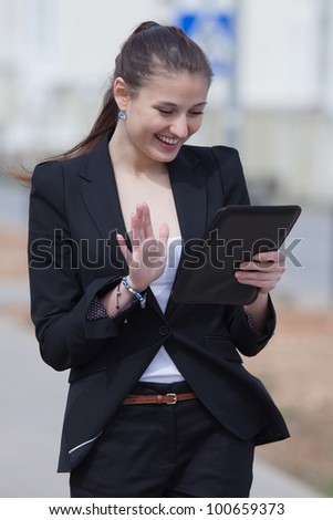 Brunette with tablet on open air. Young woman in black suit looking at screen of tablet smiling outdoors