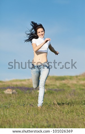 Brunette runs on open air. Barefoot young woman in jeans is running along field