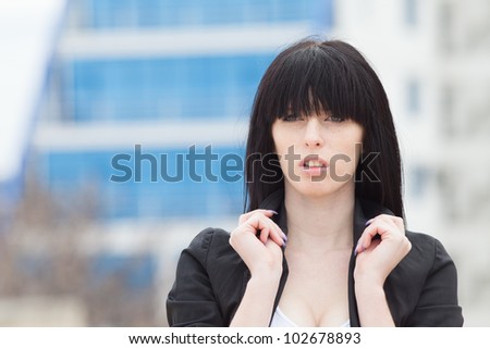 Portrait of attractive brunette on open air. Dark haired girl in black jacket holding her collar looking at camera