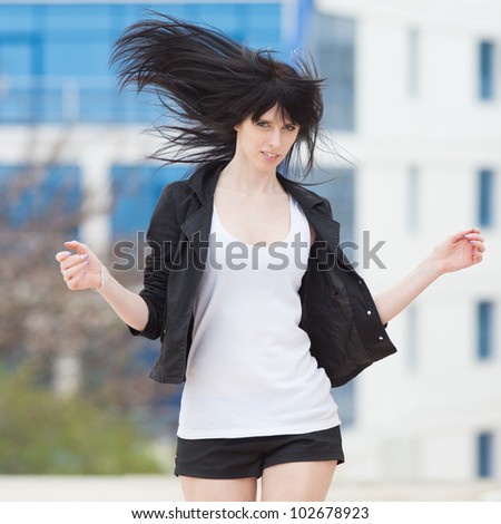 Attractive brunette in black on open air. Young woman in black shorts and jacket runs along the street with arms raised
