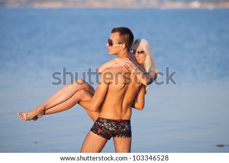 Attractive couple at the sea. Young man in swimming trunks carrying blondie on background of sea