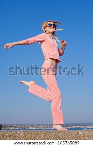 Attractive young woman in pink sportswear running on background of sky. Barefoot girl in sunglasses on open air