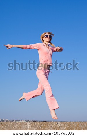 Attractive young woman in pink sportswear running on background of sky. Girl in sunglasses on open air