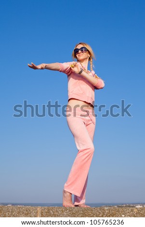 Attractive young woman in pink sportswear posing on background of sky. Girl in sunglasses on open air