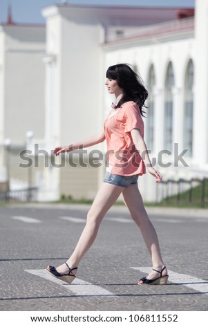 Brunette in shorts on open air. Attractive young woman in shorts walking along the crosswalk