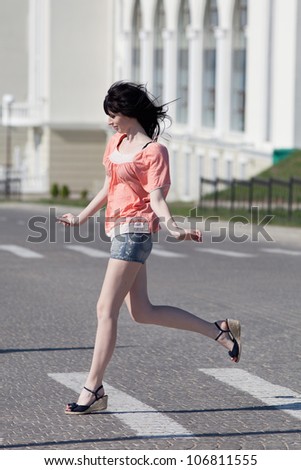 Brunette in shorts on open air. Attractive young woman in shorts running along the crosswalk