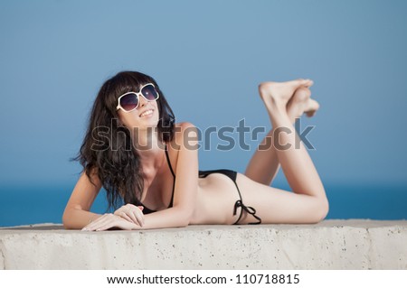 Brunette in black swimwear lying on front on open air. Young woman tans on open air