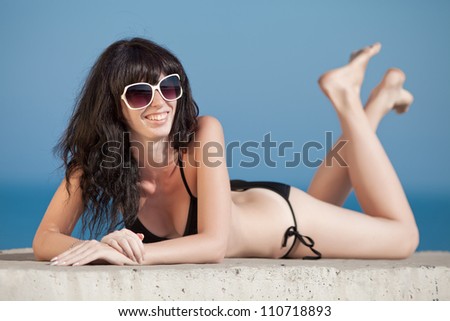Brunette in black swimwear lying on front on open air. Young woman tans on open air