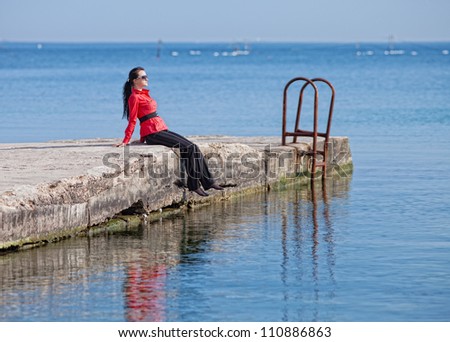 Seascape with young woman in red. Brunette in a red blouse sitting on the pier at the sea