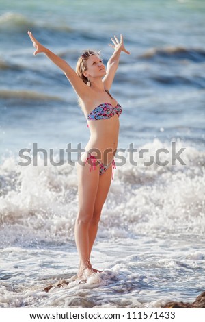 Girl at the sea. Attractive young woman with hands raised standing in line of surf
